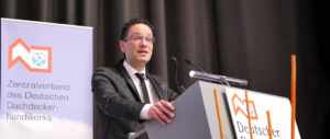 Ein Mann im Anzug spricht an einem Rednerpult mit Mikrofonen, hinter ihm ein dunkler Vorhang.