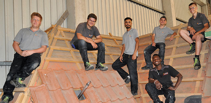 Bild: sechs Dachdecker-Lehrlingn auf einem Dach-Übungsmodell mit Ziegeln