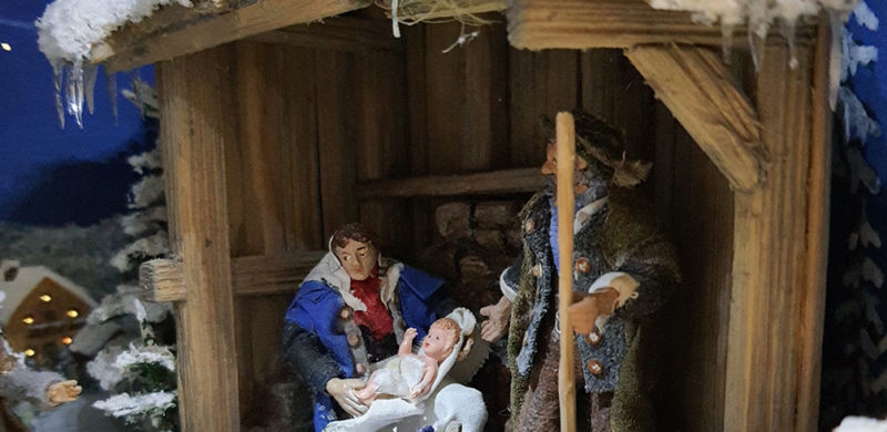 Weihnachtskrippen-heilige-Familie-Hero Eine Weihnachtskrippe mit Figuren von Maria, Josef und dem Jesuskind in einer traditionellen Holzkrippe.