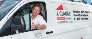 Ein Mann sitzt am Steuer eines weißen Lieferwagens, zeigt Daumen hoch und lächelt. Auf der Tür steht "J. CLA" mit Dachdecker-Logo und Kontaktdaten.