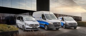 Drei silberne und blaue Mercedes-Transporter stehen vor einem modernen Bürogebäude mit Glasfassade.