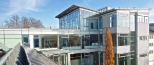 Modernes Bürogebäude mit Glasfassade und mehreren Etagen, reflektiert den Himmel, große Fenster, zeitgenössische Architektur, Blick auf das Innere und Außenbereich.