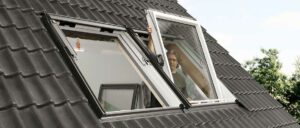 Eine Person öffnet ein Dachfenster an einem Haus mit dunkelgrauen Dachziegeln.