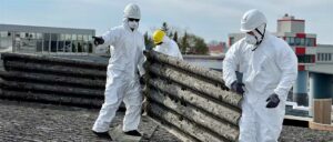 Arbeiter mit gelbem Helm und Schutzanzug entfernt alte, beschädigte Wellplatten vom Dach.