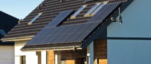 Solarmodule sind auf dem Dach eines Hauses installiert, das schwarze Ziegel hat. Es gibt auch Fenster auf dem Dach.