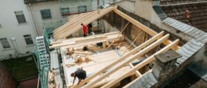 Holzkonstruktion eines Gebäudes mit sichtbaren Balken, Werkzeugen und einer Leiter im Hintergrund. Renovierungs- oder Bauarbeiten finden in einem Innenraum statt.