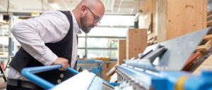 Ein Mann mit Brille arbeitet konzentriert in einer hellen Werkstatt an einer Maschine.