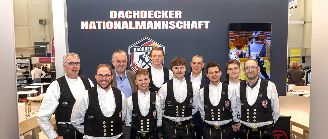 Drei junge Männer in traditioneller Zunftkleidung stehen vor einem Schild mit der Aufschrift "DECKER MANNSCH".