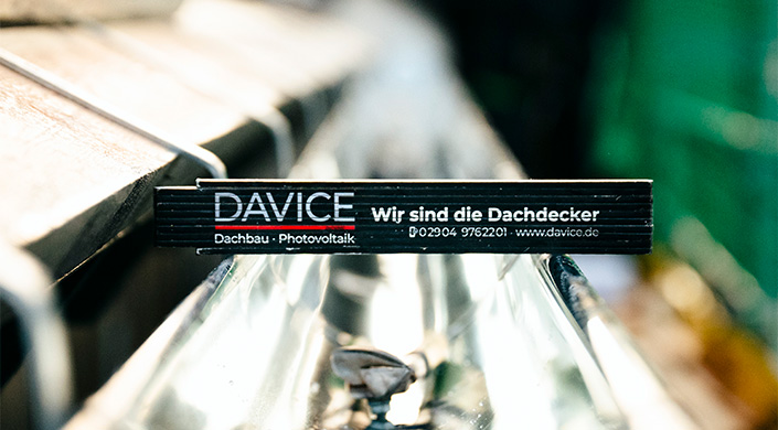 Schwarzes Schild mit wei&szlig;er Aufschrift &bdquo;Wir sind die&ldquo; und teils sichtbarer Telefonnummer, unscharfer Hintergrund mit metallischen und reflektierenden Oberfl&auml;chen.