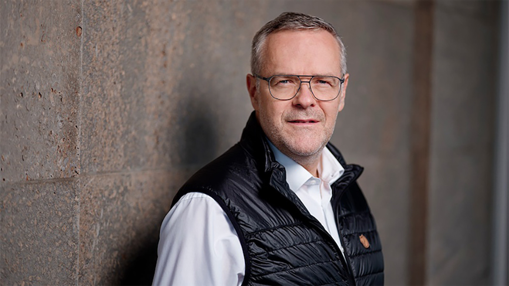 Ein Mann mit Brille und grauen Haaren tr&auml;gt eine schwarze Weste und ein wei&szlig;es Hemd, Hintergrund unscharf.