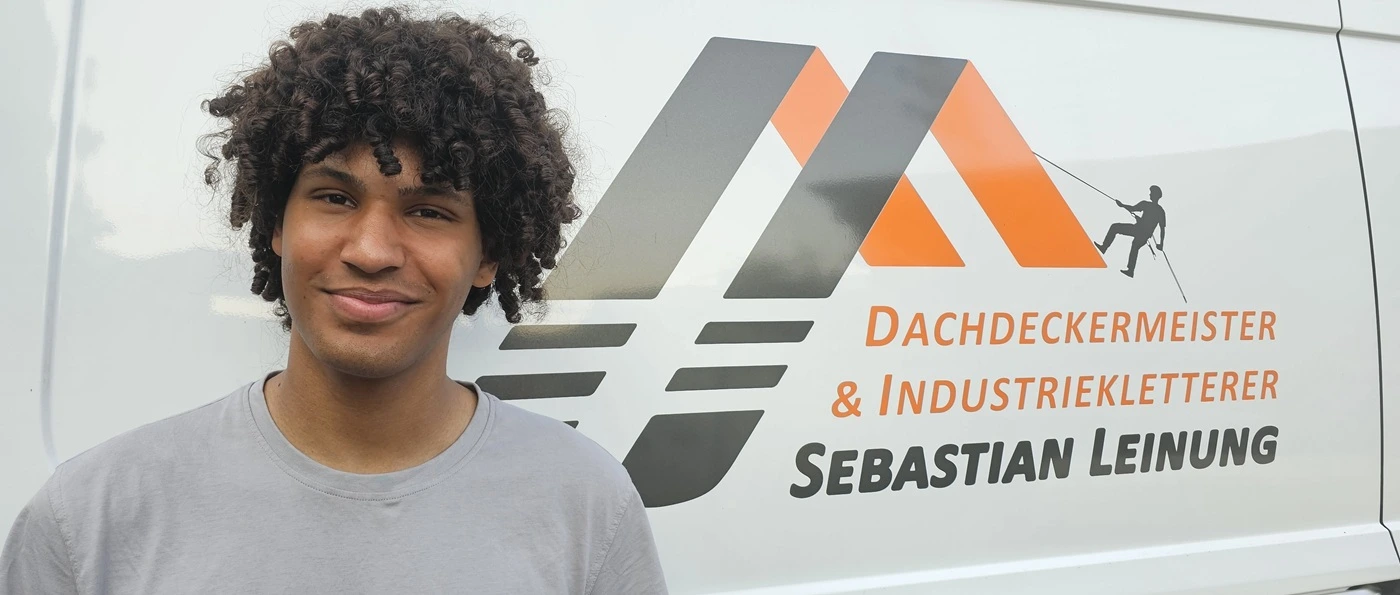 Dachdecker Malcom Mahn steht vor einem weißen Firmenwagen mit dem Logo des Betriebs Leinung.