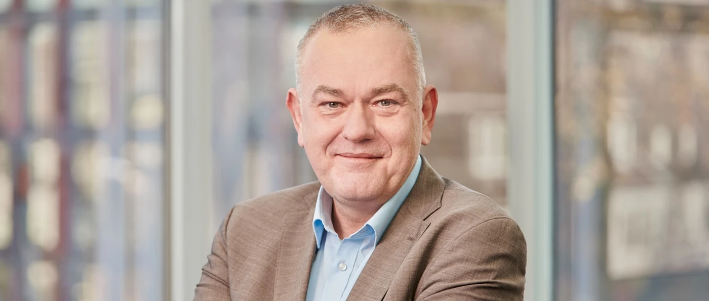 ZVDH-Präsident Dirk Bollwerk im Anzug mit blauem Hemd lächelt in einem modernen Büro mit großen Fenstern im Hintergrund.