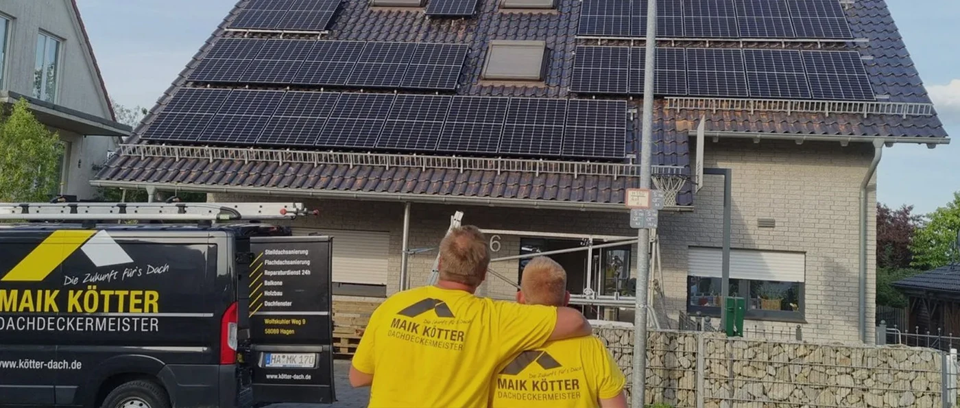 Zwei Dachdecker in gelben Shirts schauen auf ein Haus mit vielen Solarpanels, daneben steht ein Firmenwagen von Maik Kötter Dachdeckerei.