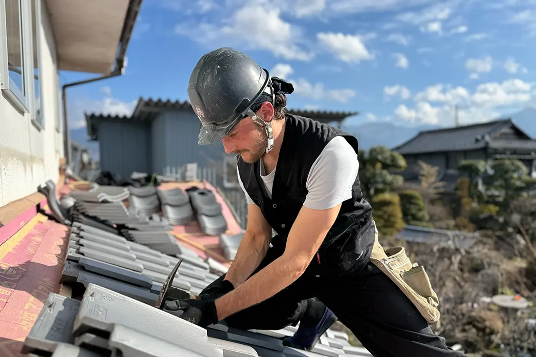Ein Bauarbeiter mit Schutzhelm arbeitet im Freien bei sonnigem Wetter, gebückt über eine Baustelle.