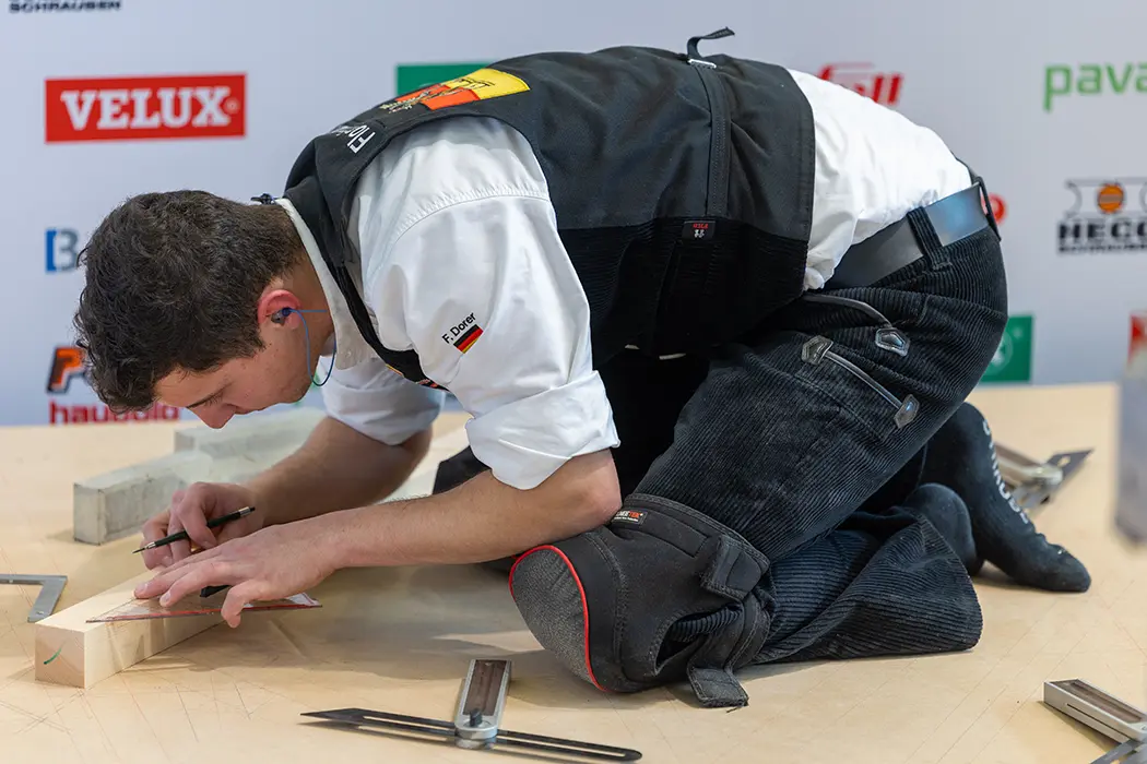 Ein Mensch mit weißem Hemd und schwarzem Schuh sitzt an einem Tisch, Details von Arm, Schuh und Kleidung sind sichtbar.