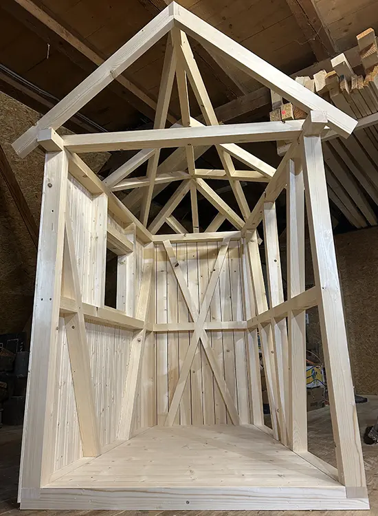 Holzkonstruktion mit sichtbaren Balken und Latten, vermutlich Teil eines Dachstuhls oder einer Holzhütte, mit Kreuzverstrebungen zur Stabilisierung.