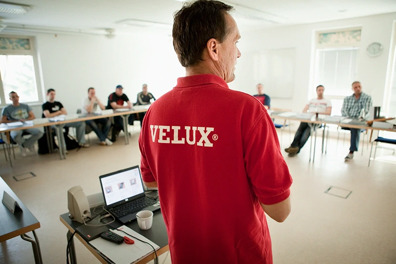 VELUX Seminare Ein Mann in einem roten Poloshirt mit dem weißen Schriftzug „VELUX“ auf dem Rücken, von hinten fotografiert.