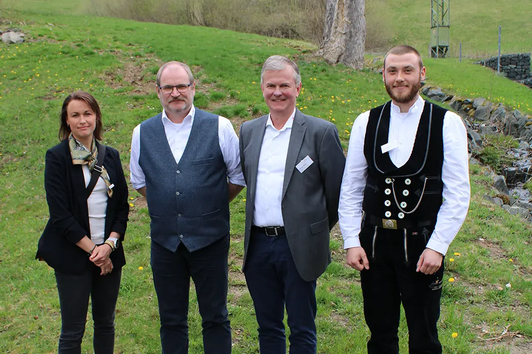 Ein Mann im Anzug steht im Freien auf einer Wiese und lächelt in die Kamera.