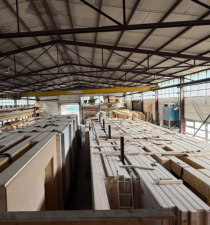 Lagerhalle mit gestapeltem Holz und Baumaterialien, Regale im Hintergrund, industrielles Dach, gut organisierter Arbeitsbereich.