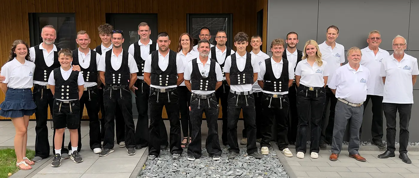 Mehrere Personen in traditioneller Handwerkerkleidung, stehen draußen auf Steinen, posieren für ein Gruppenfoto.