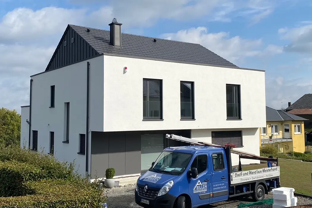 Modernes weißes Gebäude mit großem Fenster und einem blauen Transporter mit Leiter auf dem Dach, sonniges Wetter.