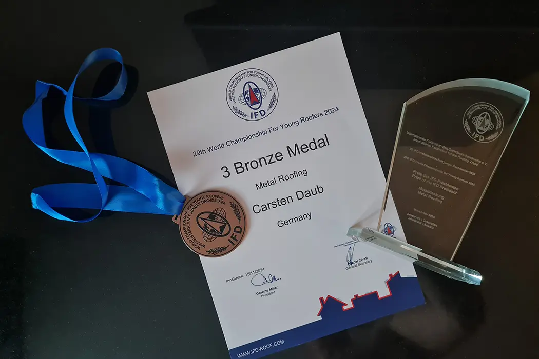 Ausschnitt einer Urkunde mit bronzener Medaille für das Metalldachdecker-Handwerk, IFD-Logo und Unterschrift des Präsidenten.