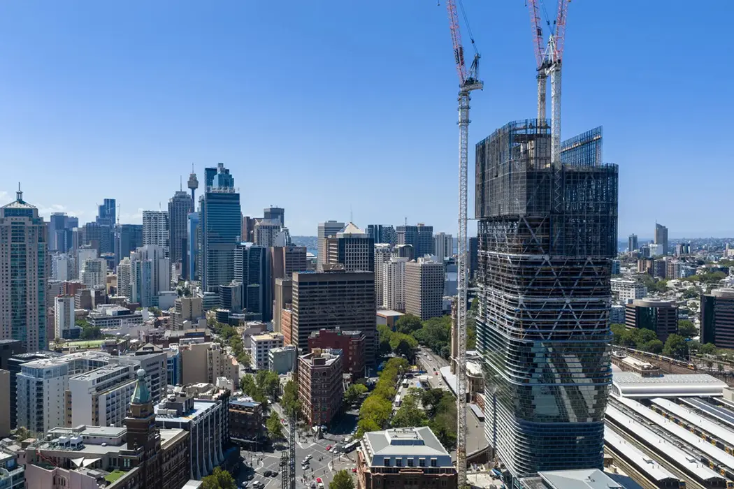 Hohe Gebäude und grüne Bäume in einer modernen Stadt unter klarem, blauem Himmel.