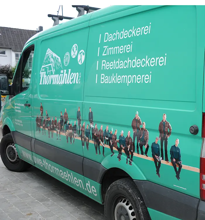 Die Seite eines grünen Firmenwagens mit weißer Schrift und einer Illustration von Menschen, die auf einem Holzbalken sitzen.