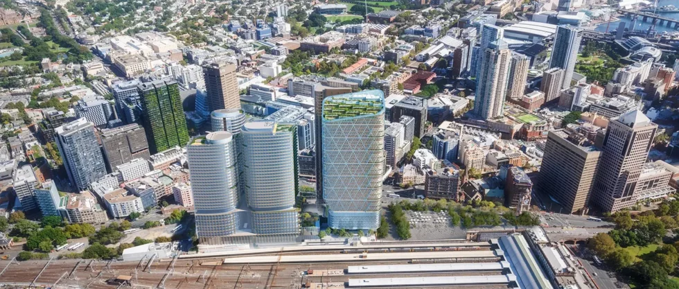 Hohes modernes Gebäude mit begrüntem Dach und geometrischem Fassadenmuster, umgeben von Stadt und Bahngleisen.