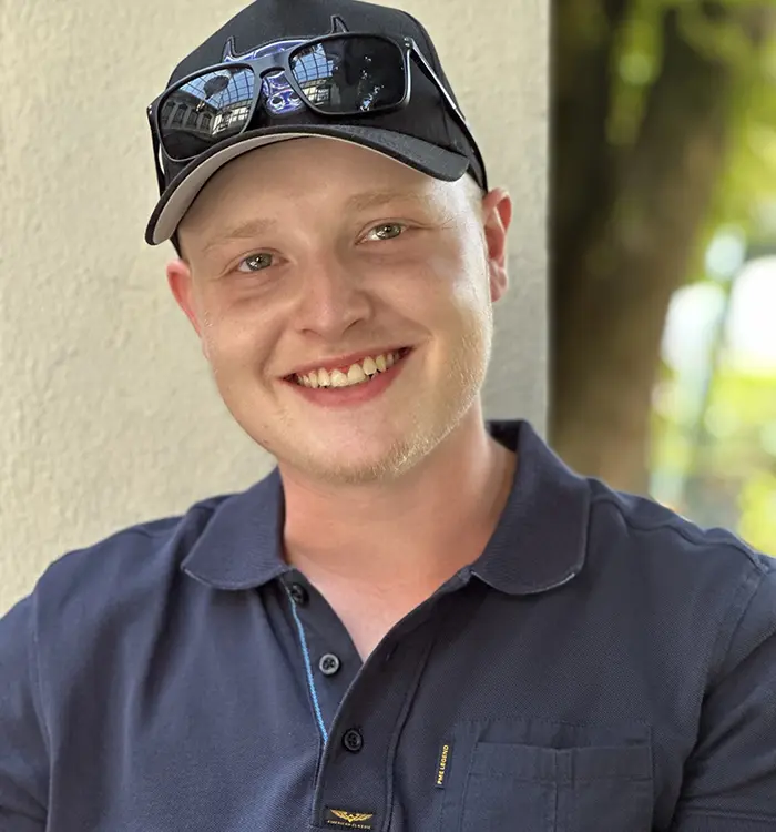 Nahaufnahme eines lächelnden Julien Brinker mit blonder Gesichtsbehaarung, schwarzer Kappe und Sonnenbrille auf dem Kopf.