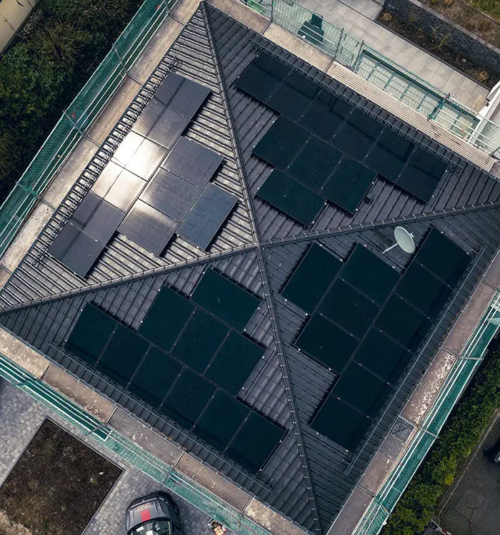 Schwarze Solarpanels sind auf einem schrägen, dunkelgrauen Metalldach montiert, fotografiert aus der Vogelperspektive.